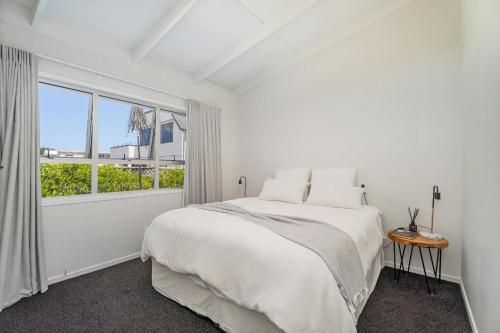 a white bedroom with a bed and a window at Beachside on Hinemoa in Whangamata