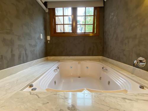 a large white tub in a room with a window at Pousada Stillo Gramado Centro - 300 metros da rua coberta in Gramado