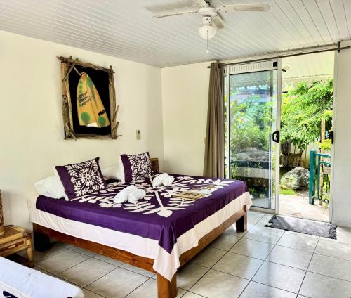 a bedroom with a bed with purple sheets and a window at Relais Fenua in Punaauia