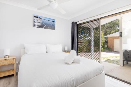 a white bedroom with a bed and a balcony at Callala On King - Pet Friendly - Swimming Pool in Callala Beach