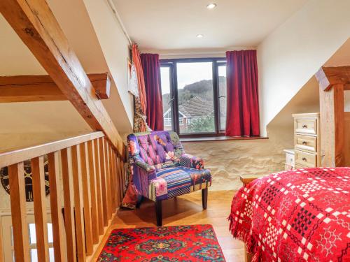 a bedroom with a bed and a chair and a window at Dovetail Cottage in Llangollen