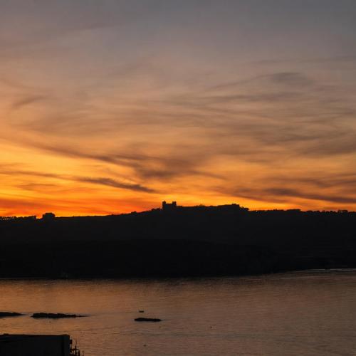 a sunset over the water with a castle in the distance at Moonlit Terrace Escape in St. Paul's Bay