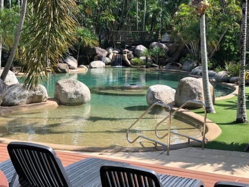 a pool of water with rocks and chairs in it at Reef Resort Villas Port Douglas in Port Douglas