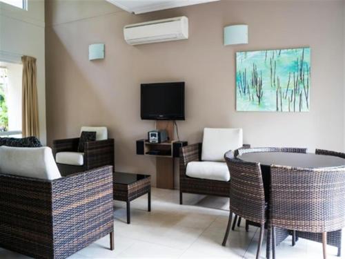 a living room with a table and chairs and a tv at Reef Resort Villas Port Douglas in Port Douglas