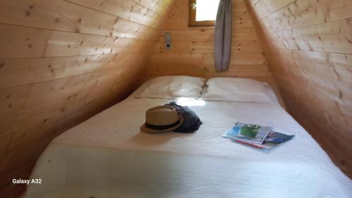 a bed with a hat and a book on it at Refuge - Les Chalets du lac Belcaire in La Celle-sous-Gouzon
