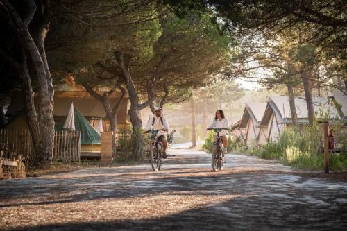 two people riding bikes down a dirt road with trees at Huttopia Lagoa de Óbidos in Casal do Narcizo