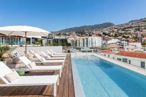 a hotel swimming pool with white lounge chairs and a view at Hotel Orquidea in Funchal