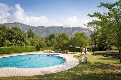 a swimming pool with people in it with mountains in the background at Huttopia Barcelona Pirineos in Guardiola de Berguedà