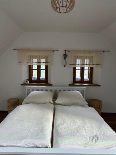 a bedroom with a large white bed with two windows at Chalupa Vlachovice in Vlachovice