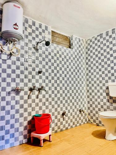a bathroom with a red bucket on a stool next to a toilet at Hotel Dev in Kainūr
