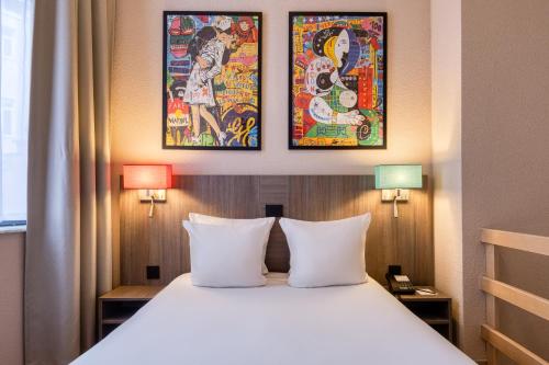 a bed in a hotel room with two paintings on the wall at ALMA Grand Place Hotel in Brussels