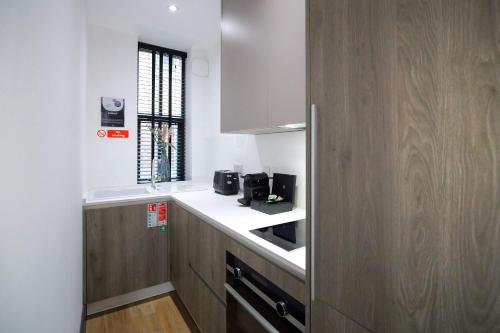 a kitchen with white counters and wooden cabinets at Stylish Northern Quarter Studio, Ideal for Leisure & Work Stays in Manchester