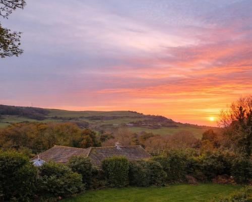 a house in a field with the sunset in the background at Hunter Heights Loft – Near Ventnor, Isle of Wight in Wroxall