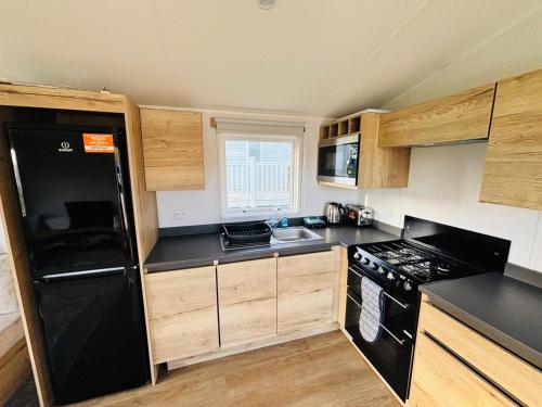 a small kitchen with black appliances and wooden cabinets at Shamrocks Cove Caravan - Award-Winning Coastal Retreat in Crantock