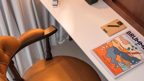 a desk with a chair next to a table with a book at Ruby Stella Hotel London by IHG in London