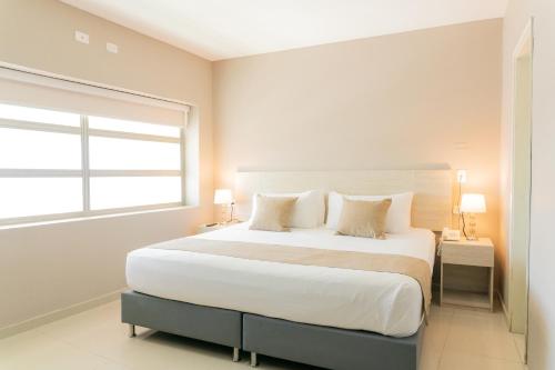 a white bedroom with a large bed and a window at Ribai Hotels - Barranquilla in Barranquilla