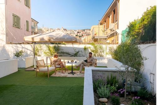 two people sitting around a table in a garden at Jacaranda Rooms in SantʼAntìoco