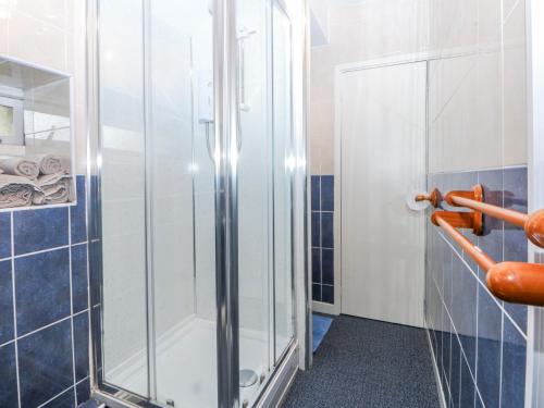 a glass shower in a bathroom with blue tiles at First Floor Apartment in Porthmadog