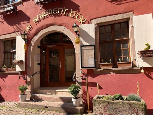 a pink building with an archway and a door at Hôtel Le Sarment d'Or in Riquewihr
