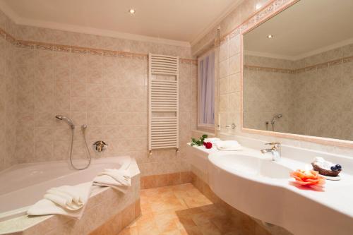 a bathroom with a tub and a sink and a mirror at Dolomites Wellness Hotel Savoy in La Villa