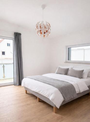 a white bedroom with a large bed and a chandelier at Horgau Living in Horgau
