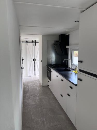 a kitchen with white cabinets and a sink and a door at Modern chalet in de bossen van de Veluwe in Epe