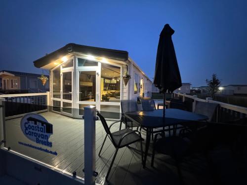 a deck with a table and chairs and an umbrella at Golden Anchor - The Milano - Coastal Caravan Breaks in Chapel Saint Leonards