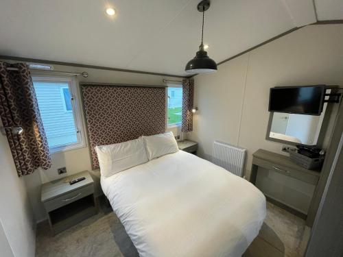 a bedroom with a white bed and a flat screen tv at Golden Palm Resort - The Atlas Family - Coastal Caravan Breaks in Chapel Saint Leonards