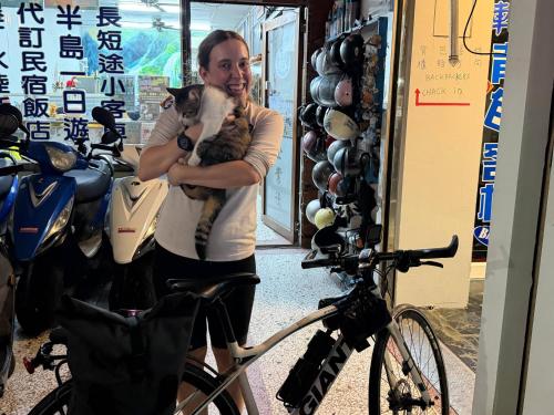 una mujer sosteniendo un gato delante de una bicicleta en 背包客棧Backpackers Hostel, en Checheng