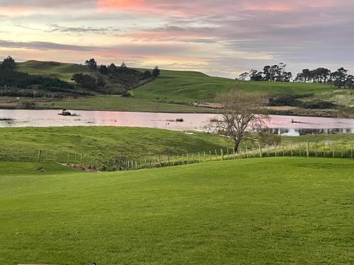 a green field with a lake and a fence at Boutique Tiny House Stargazing & Rural Views in Parore