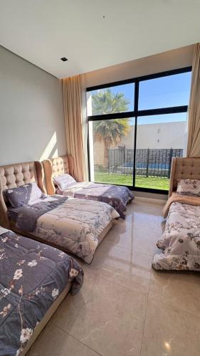 three beds in a room with a large window at شاليه ماديرا in Hail