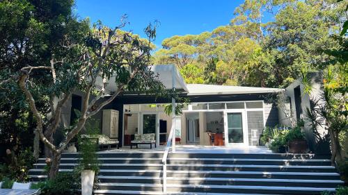 a white house with stairs in front of it at Luxury Pearl Beach House with Private Heated Mineral Pool, Yoga Deck & Fire Pit in Pearl Beach