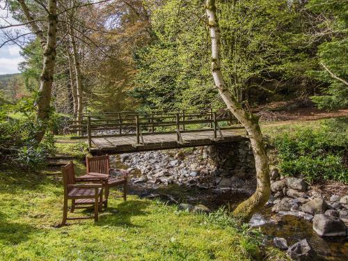 a wooden bridge over a stream with a bench and a chair at Tinkerbell in Balnaboth