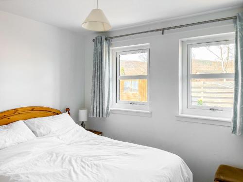 a bedroom with a white bed and two windows at Glenrothay in Aviemore