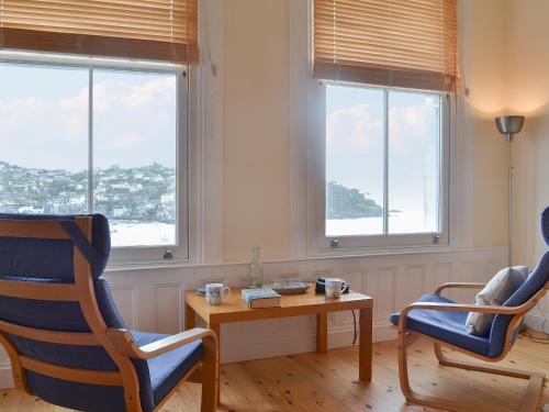 a living room with two chairs and a table and windows at Tides Reach in Fowey