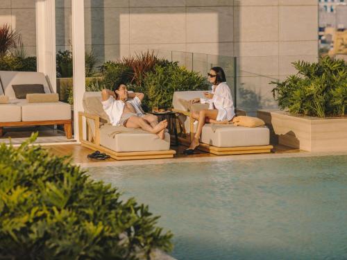 two people sitting on chairs next to a swimming pool at Fairmont Hanoi in Hanoi