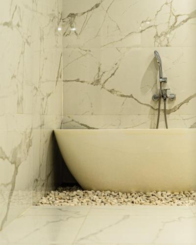 a bathroom with a bath tub sitting on a pebble floor at Nio Garden Hotel in Sumbawa Besar