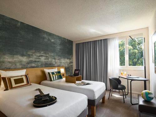 a hotel room with two beds and a desk at Novotel Bayeux in Bayeux