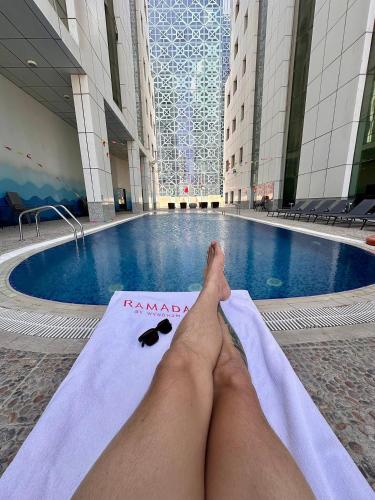 a person laying on a towel in front of a swimming pool at Ramada by Wyndham Doha Old Town in Doha