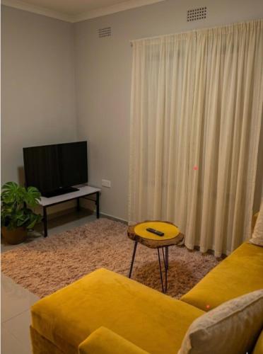 a living room with a yellow couch and a flat screen tv at DeltaGateway selfcatering in Maun Airport