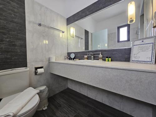 a bathroom with a toilet and two sinks and a mirror at Penélope Hotel in Ialysos