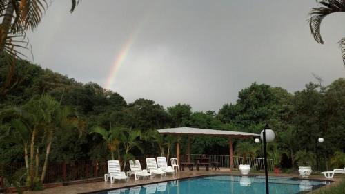 a pool with chairs and a rainbow in the background at Pousada Vale da Serra in Serra Negra