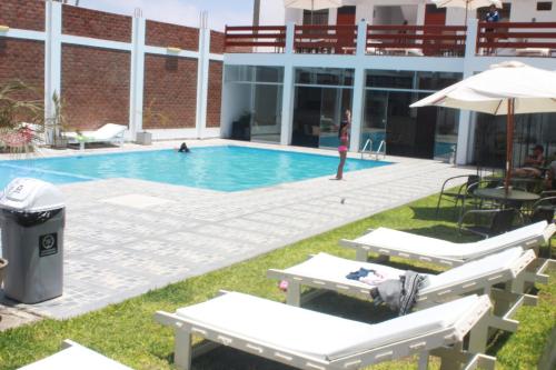 una piscina con sillas y sombrilla en Hotel Residencial Los Frayles, en Paracas