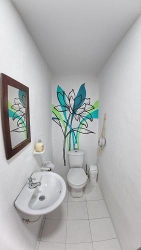a bathroom with a toilet and a sink with a flower on the wall at Hostal Bambu in San Agustín