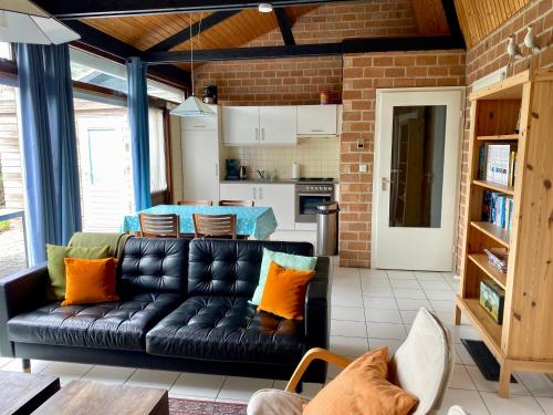 a living room with a black leather couch and a kitchen at Boerenslag 46 in Sint Maartenszee