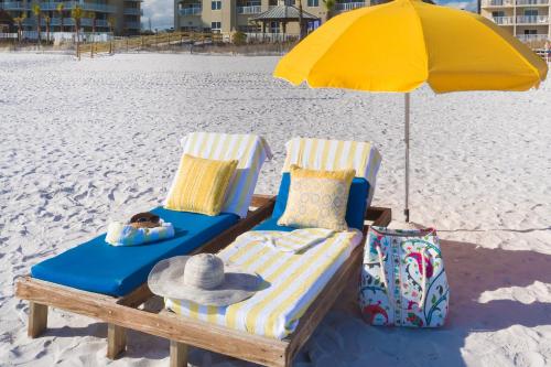 two beach chairs and an umbrella on the beach at Escapes! To The Shores Orange Beach, A Ramada by Wyndham in Orange Beach