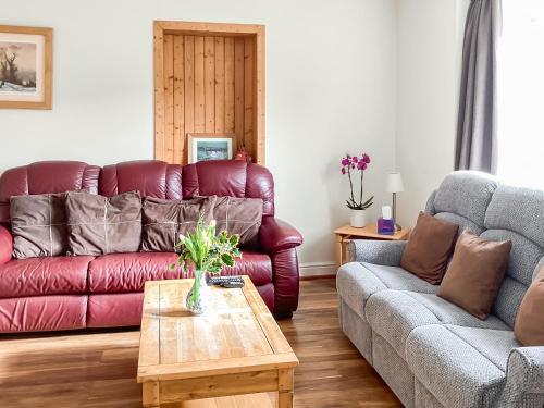 a living room with a red leather couch and a table at Keepers Cottage - Uk51549 in Kirktown of Auchterless