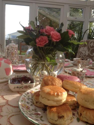 a plate of pastries on a table with a vase of roses at The Inglenook Hotel in Bognor Regis