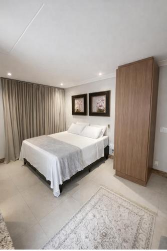 a bedroom with a white bed and a wooden cabinet at Sun Square Suítes By Temporada Gyn in Goiânia
