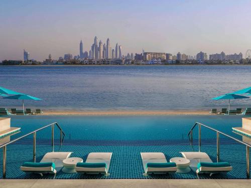 a swimming pool with chairs and umbrellas and a city at The Retreat Palm Dubai MGallery by Sofitel in Dubai